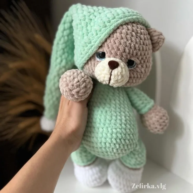 Plush crochet teddy bear in mint green pajamas and a long sleeping cap, held in a hand